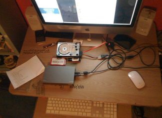 Cara Kembalikan Data Yang Hilang Computer desk with hard drives, cables, and keyboard; data recovery setup.