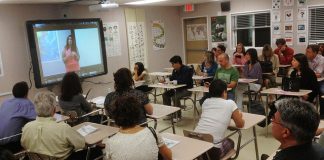 Muat Turun Video dari Internet Classroom of adults watching a video presentation on a large screen.