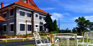 Rumah Peranginan Untuk Kakitangan Awam Stone building with red roof, surrounded by landscaping and white metal patio furniture.