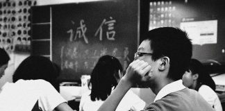 Bina Kuiz Dengan Perisian Mudah Students in a classroom, one student thoughtfully rests their chin on their hand. Blackboard shows Chinese characters.