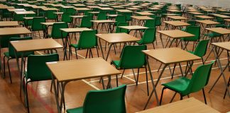 Julat Gred Baru Peperiksaan dan Ujian Empty examination hall with rows of desks and green chairs ready for exams.