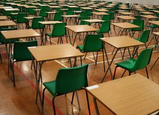 Julat Gred Baru Peperiksaan dan Ujian Empty examination hall with rows of desks and green chairs ready for exams.