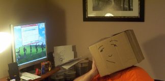 Lajukan Komputer Yang Lambat Person with cardboard box on head sits at messy computer desk, looking at screen showing slow computer message. Lajukan Komputer.