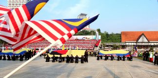 Himpunan Bahan dan Idea Sambutan Kemerdekaan Di Sekolah Malaysian flag bearers at a school Independence Day celebration. Students kneel holding large flags.