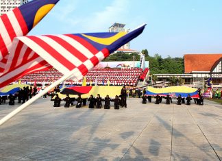 Himpunan Bahan dan Idea Sambutan Kemerdekaan Di Sekolah Malaysian flag bearers at a school Independence Day celebration. Students kneel holding large flags.