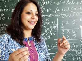 Smiling female math teacher explaining equations on a chalkboard.