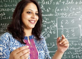 Web dan Aplikasi Mengira Soalan Matematik Smiling female math teacher explaining equations on a chalkboard.