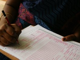 Close-up of hands filling out an OMR answer sheet with a red pencil.