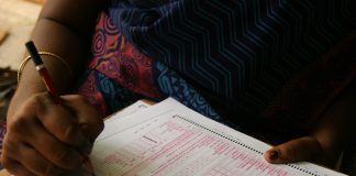 Semak Kertas Jawapan OMR dengan Mudah Close-up of hands filling out an OMR answer sheet with a red pencil.