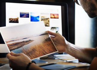 Aplikasi Percuma Untuk Edit Gambar dan Foto Person reviewing a landscape photo print, comparing it to images on a computer screen. Free photo editing app.