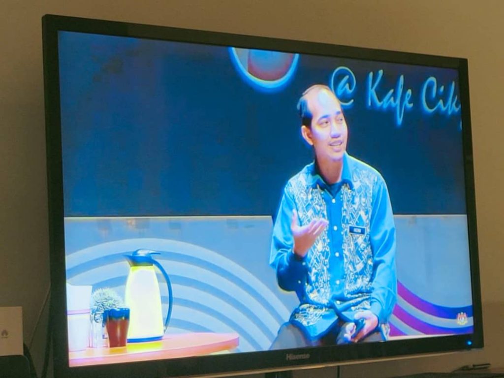 Man speaking on a TV show, "@ Kafe Cik" displayed